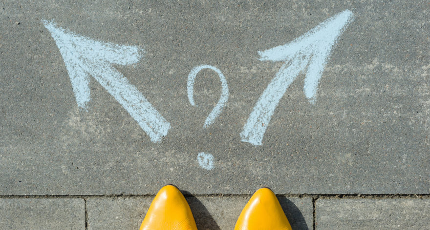 The tips of yellow pointed shoes in front of two chalk arrows pointing both left and right with a question mark between them.