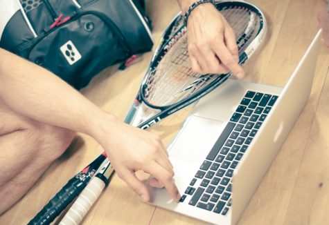 Two squash players with their equipment gathered around a laptop computer.