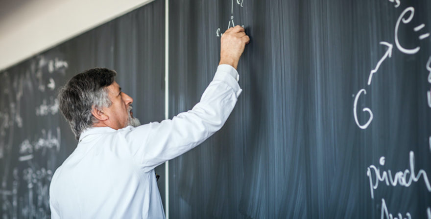 A teacher writing formulas on a chalk board.