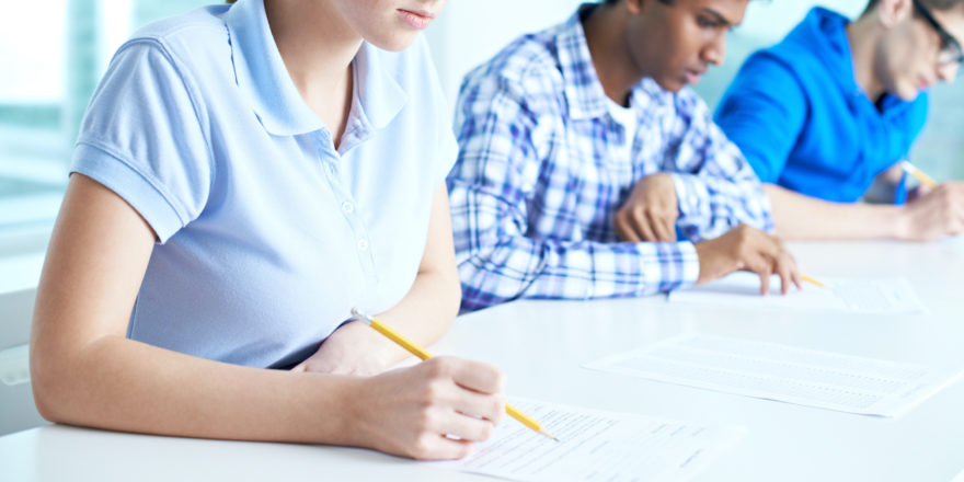 Several students taking tests on a long white table.