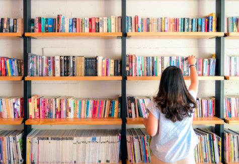 A female perusing through many books stacked on a wall full of bookshelves.