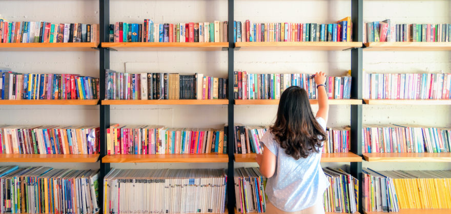 A female perusing through many books stacked on a wall full of bookshelves.