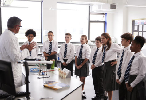 A group of private school students around their chemistry teachers desk.