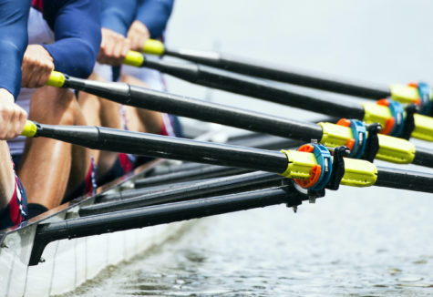 A Crew team practicing on a body of water with the focus on their oarlocks.
