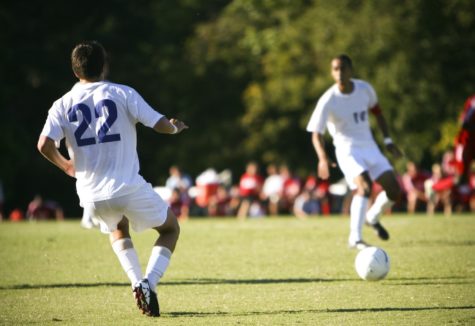 Two soccer teammates passing the ball in the middle of a soccer match.