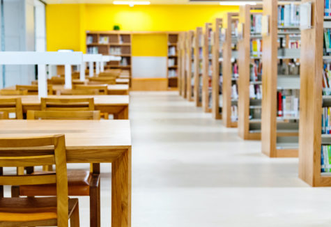 Looking down the walkway of a college library with shelves on the right and reading desks on the left.