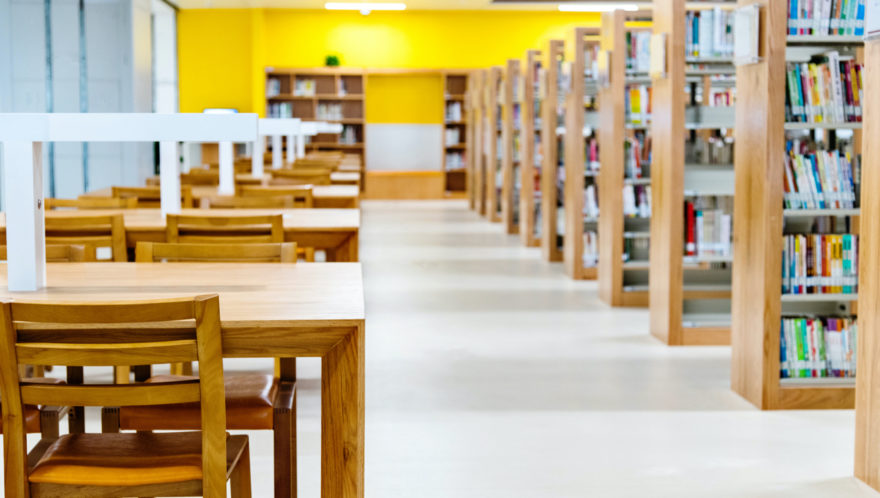 Looking down the walkway of a college library with shelves on the right and reading desks on the left.