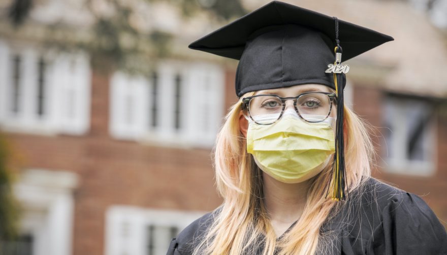 A 2020 graduate in her cap and gown wearing a yellow protective face mask.