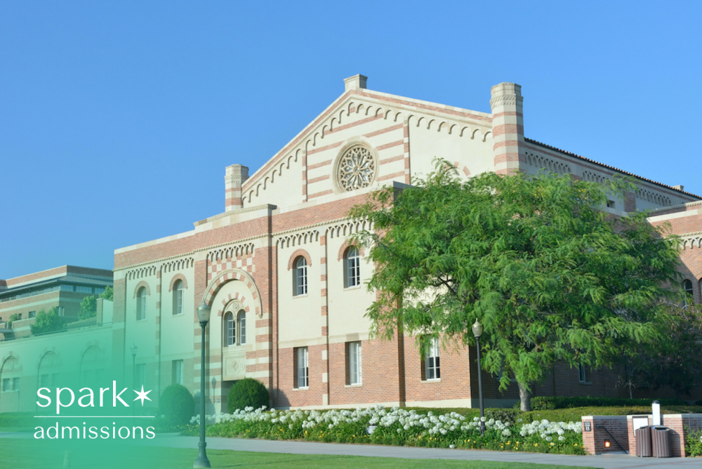 Historic college academic building with brick architecture, landscaped grounds, and a clear blue sky on a university campus.