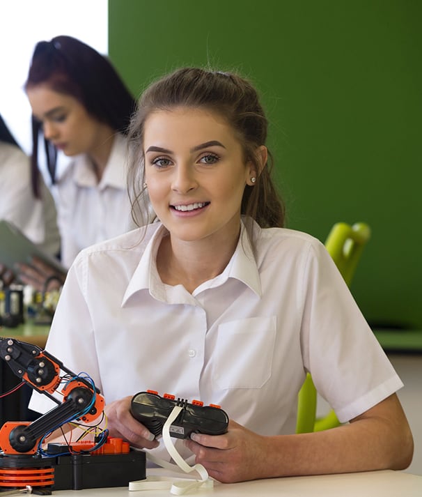 Smiling brunette teen girl in private school uniform seated in science lab with robotics equipment