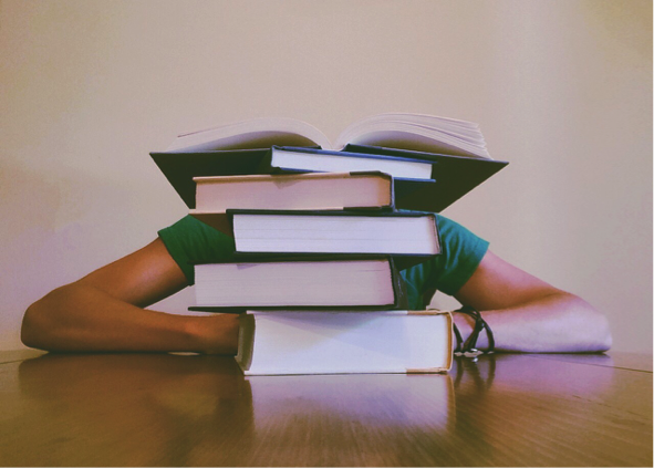 A student hidden behind a stack of AP and IB textbooks.