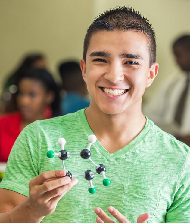 Smiling teen boy of Asian descent holding molecular model in classroom