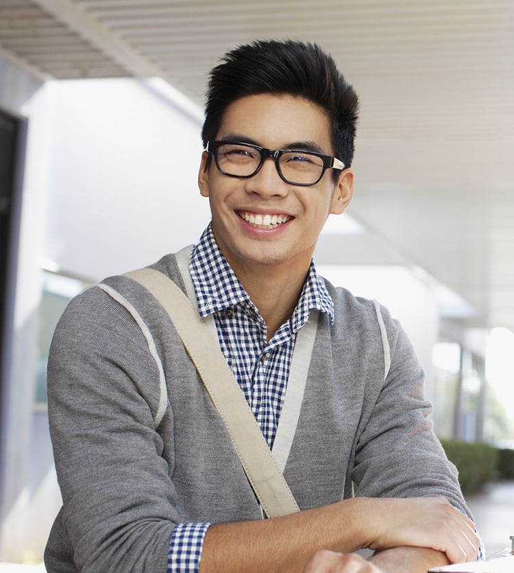 Smiling Asian teen boy wearing glasses sitting at table outside school