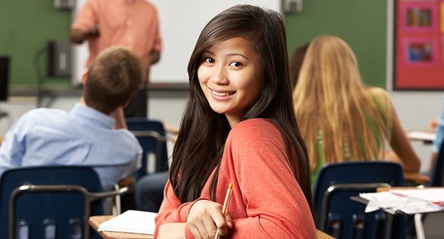 A closeup on a teenage female student in a classroom turning in her desk seat to look at you.