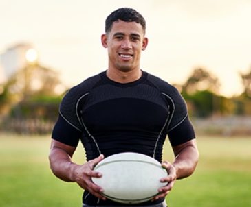 Smiling college rugby player standing on field holding rugby ball