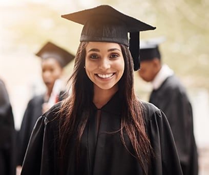 Smiling high school girl of Indian descent wearing graduation cap and gown with classmates in background