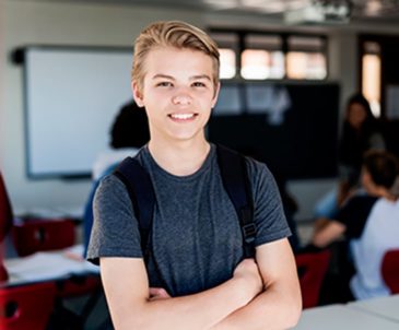 Smiling young blonde teen boy standing in classroom