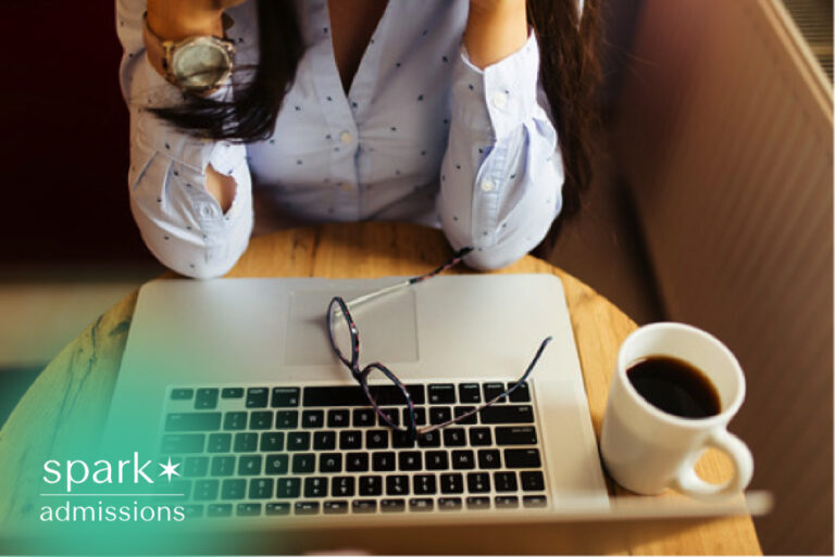 Student sitting at a laptop with coffee and eyeglasses, looking stressed while reviewing coursework or preparing for an online exam.