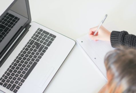 A woman taking notes in a notebook while working on a laptop.