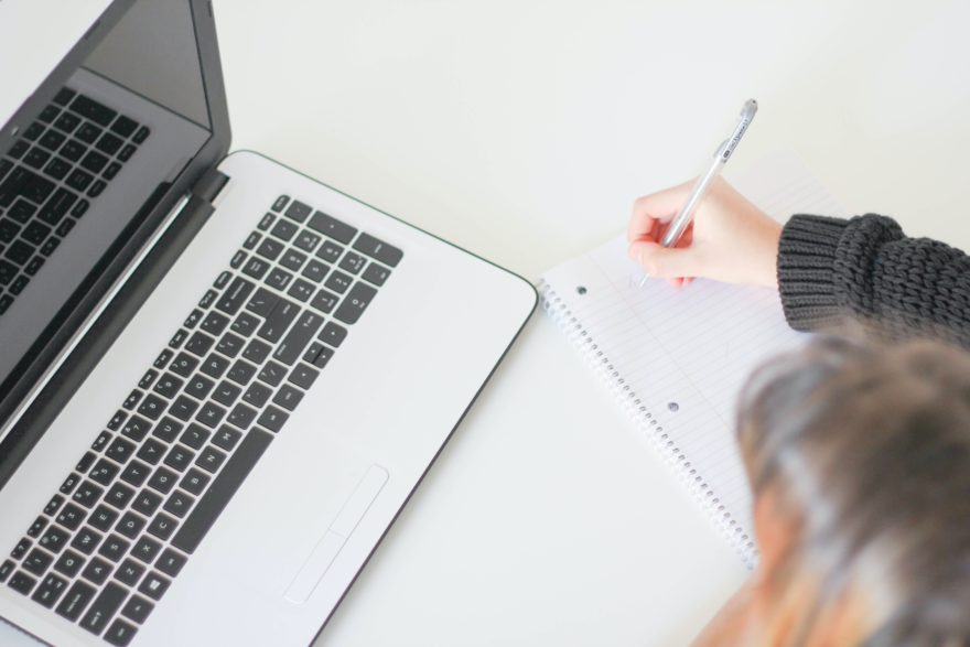 A woman taking notes in a notebook while working on a laptop.