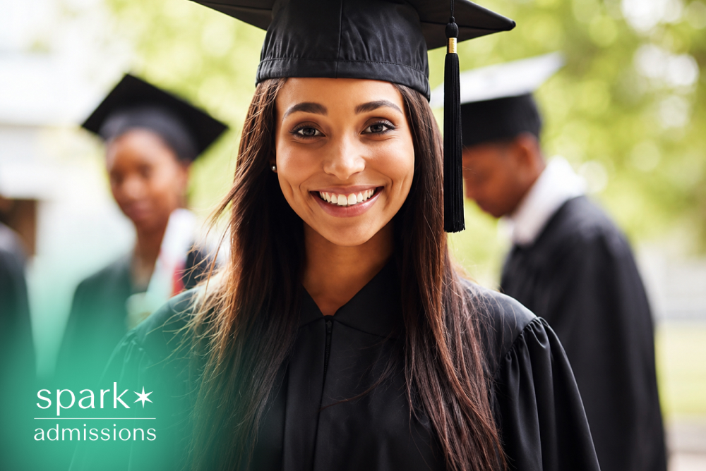 Smiling college graduate wearing a cap and gown during commencement ceremony with classmates in the background.