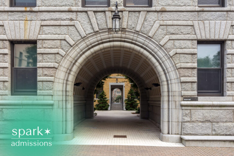 Historic stone archway entrance connecting university buildings on a landscaped campus walkway.