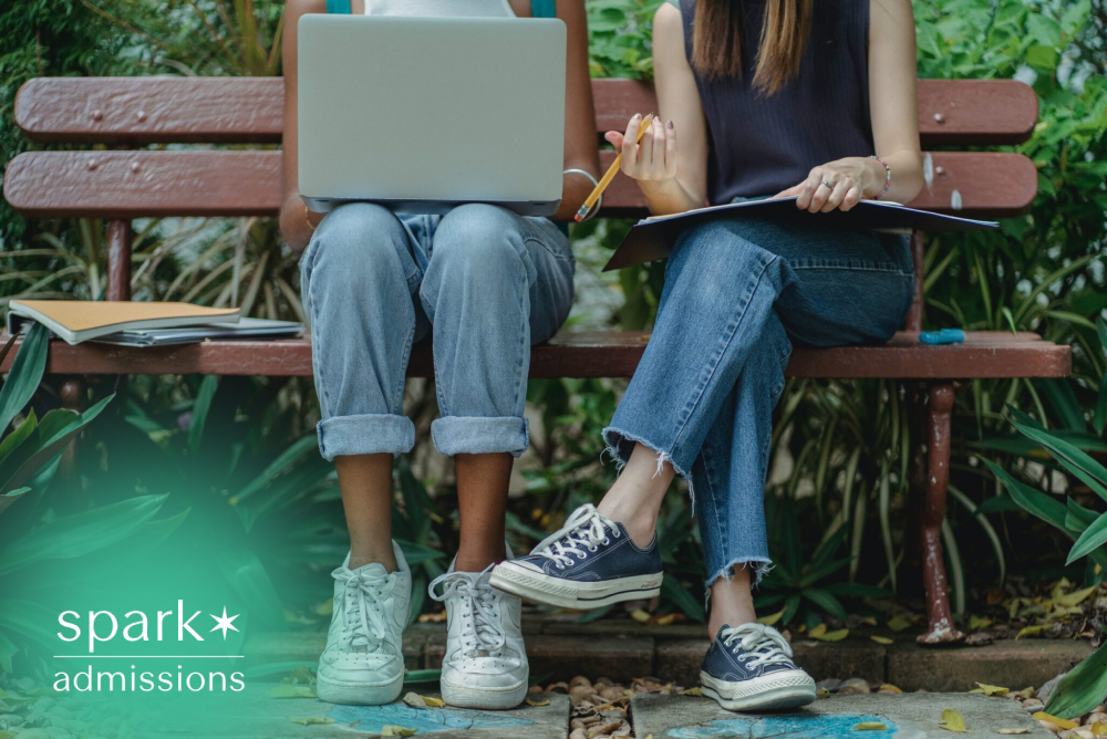 Two students studying together outdoors on a campus bench using a laptop and notebook.