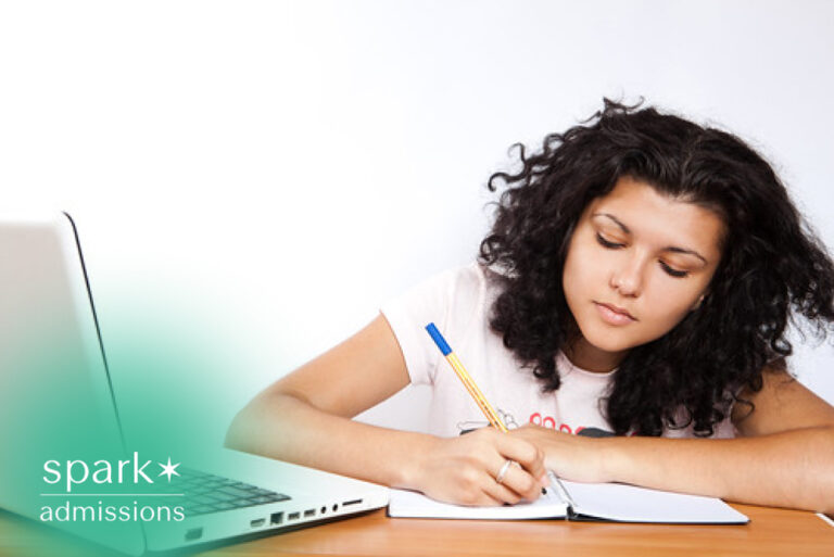 Student writing notes in a notebook beside a laptop during an at-home study session.