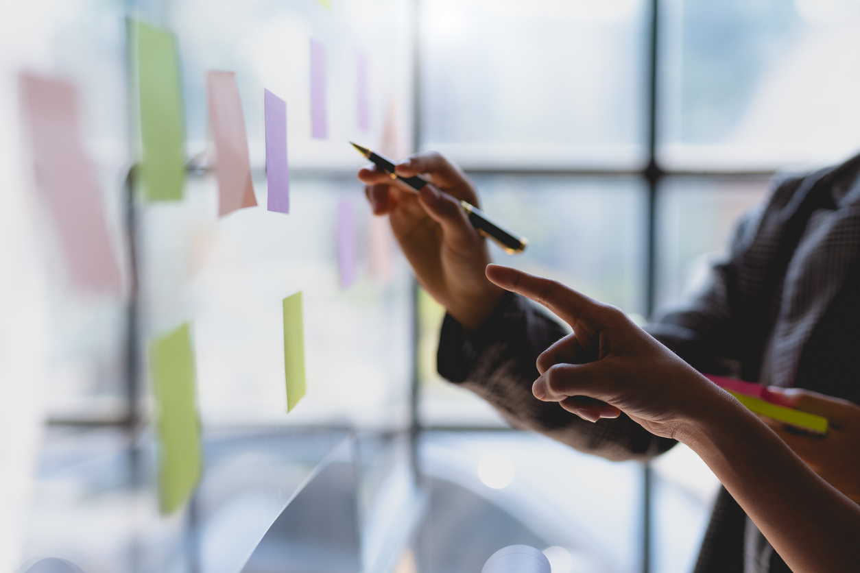 Team business people writing planning and brainstorming putting sticky notes on glass wall in the office.