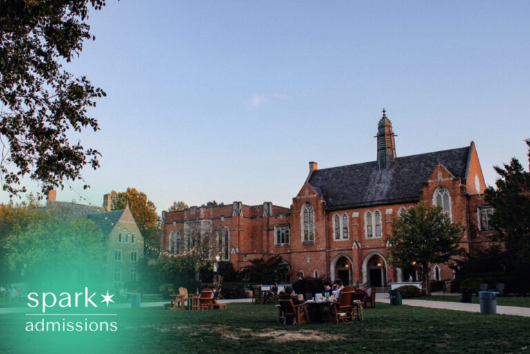 Historic university campus quadrangle with Gothic-style academic buildings, students relaxing on the lawn, and an inviting collegiate atmosphere at dusk.
