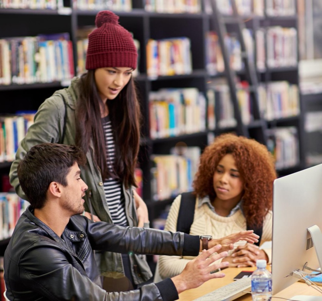 Three college students working together at a computer in a library