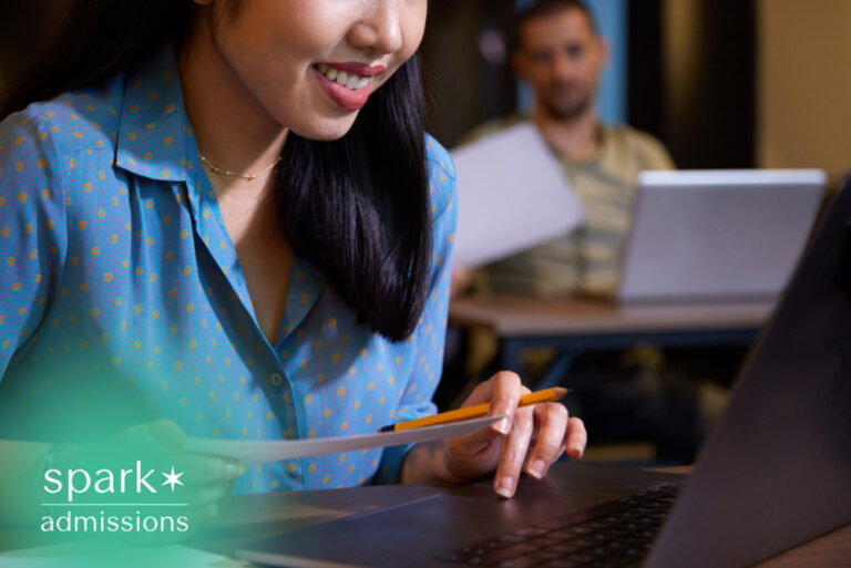 Student reviewing college admissions documents on a laptop while holding paperwork and a pencil, representing online application review, admissions decisions, and enrollment preparation.