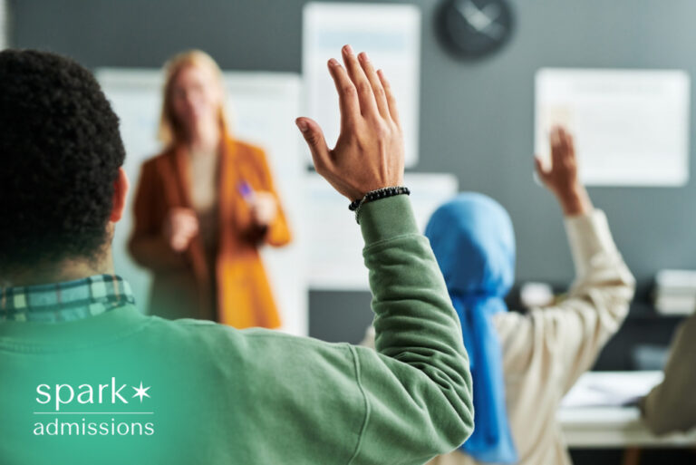 Diverse college students raising their hands during a classroom discussion while an instructor teaches, highlighting active learning, student engagement, and collaborative education.