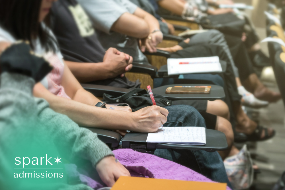Prospective college students taking notes during a college information session or admissions presentation in a lecture hall.
