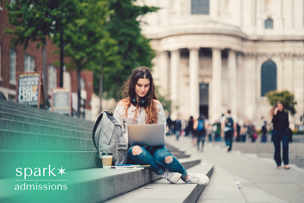 College student studying on outdoor campus steps with a laptop, backpack, and coffee while working on coursework between classes.