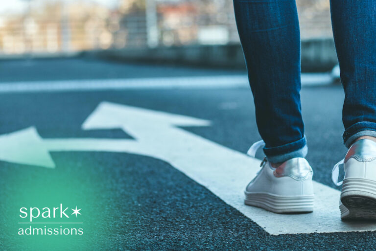 Student standing at a directional arrow on a road, symbolizing the college decision-making process, choosing the right university, and planning future academic goals.
