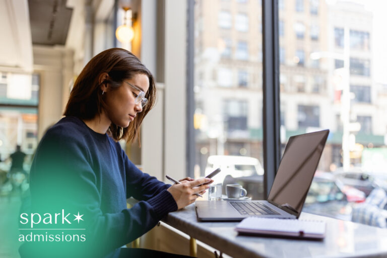 Student using a laptop and smartphone while studying in a café, researching colleges and working on college applications in a modern urban setting.
