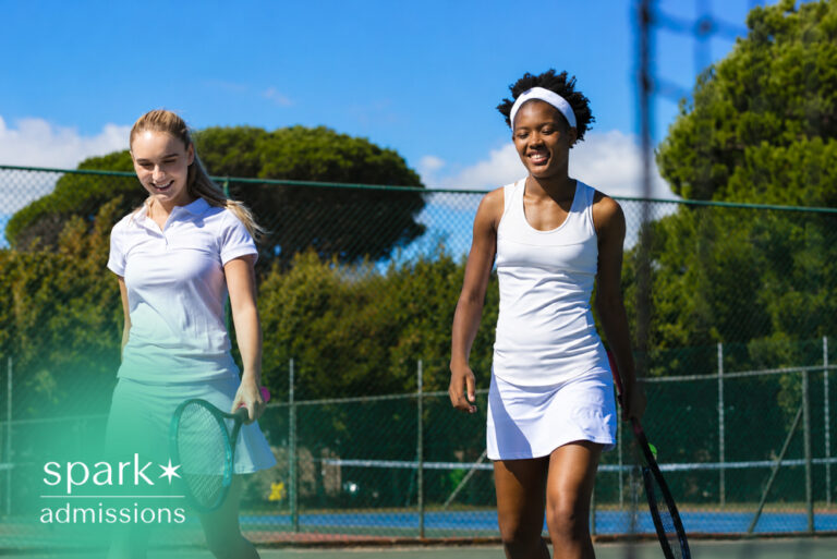 Two female high school tennis players walking across an outdoor tennis court after practice or a match.