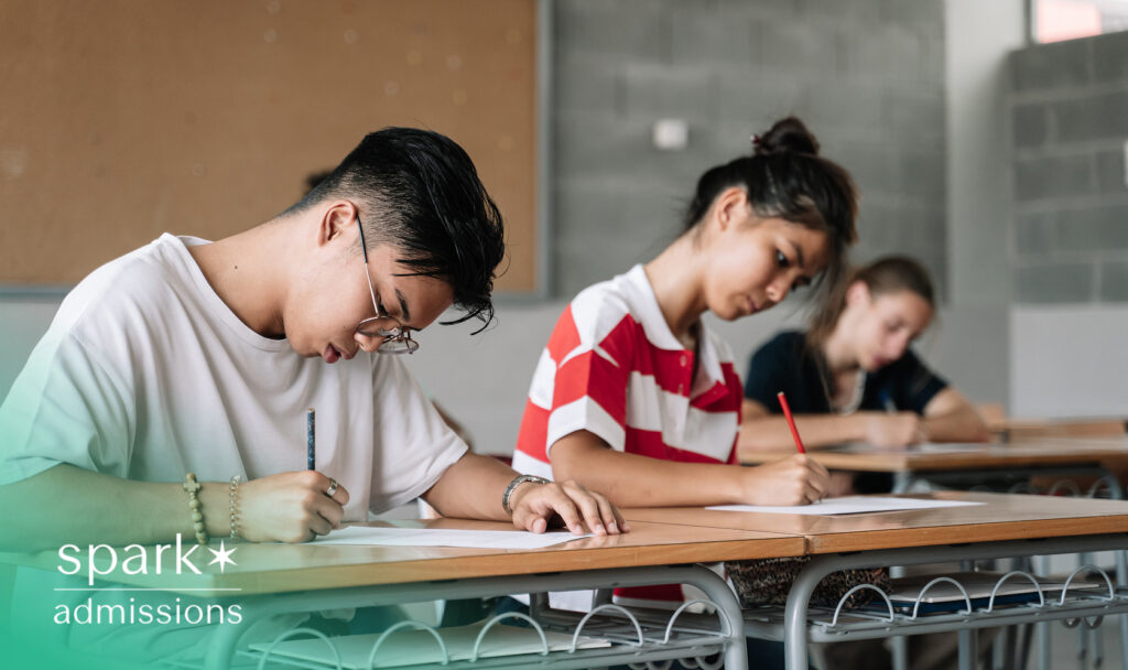 Students sitting in a classroom taking a written test, representing the academic rigor and standardized testing often involved in the college admissions process.