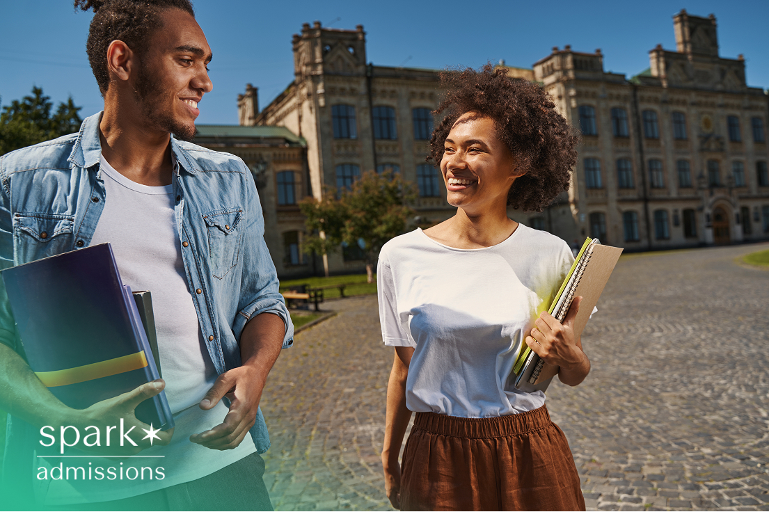 Two smiling students walking on a university campus, holding notebooks and textbooks, with historic academic buildings in the background. The image represents the vibrant campus life and opportunities offered by top economics schools.