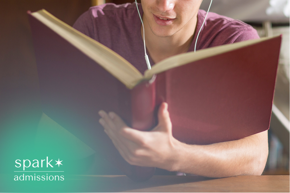 Student reading a book while listening with earbuds