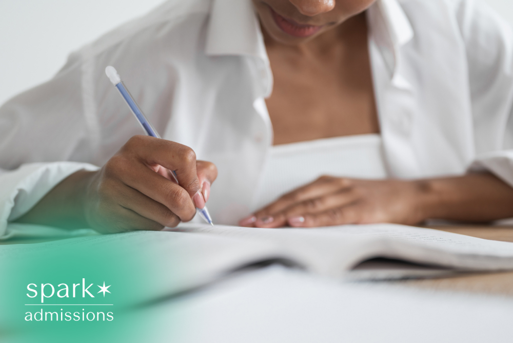 Student writing notes in an open book with a pencil