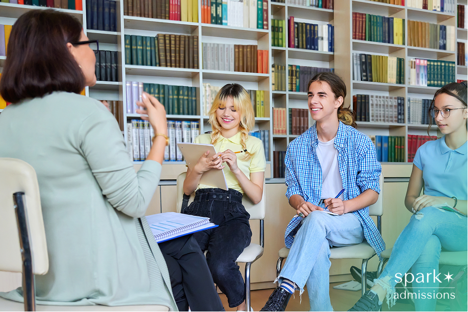 A teacher leads a group discussion with three smiling students in a library setting