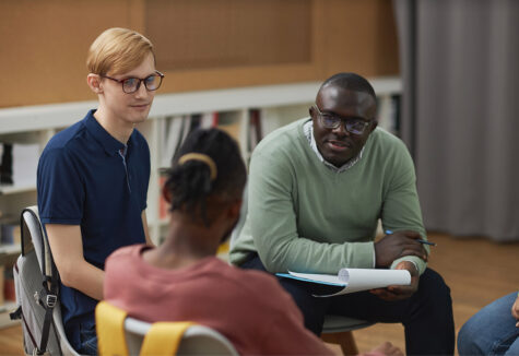 Black man as male psychologist talking to group teenagers in therapy session