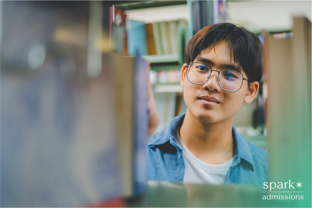 A student with glasses looks at books on a shelf in a school library