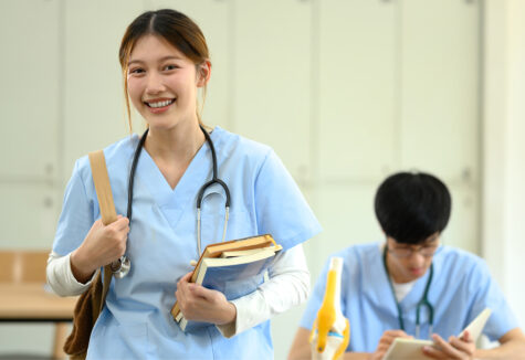 Smiling medical student in scrubs carrying books heading to class