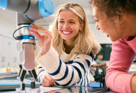 Two Female College Or University Engineering Students Using Digital Tablet To Control Robot Arm