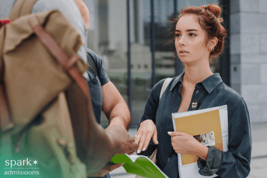 College applicant holding a large notebook while talking with peers on campus