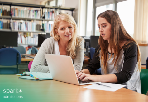 Tutor or teacher helps a student with laptop work at a library table, reviewing notes and assignments during an academic support session.