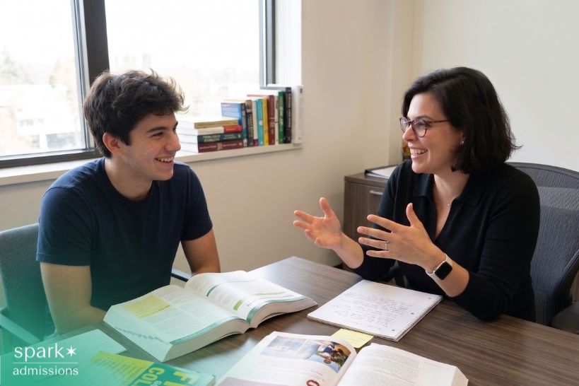 College admission consultant advising a student during a one-on-one meeting with guidebooks, notes, and application materials on the desk